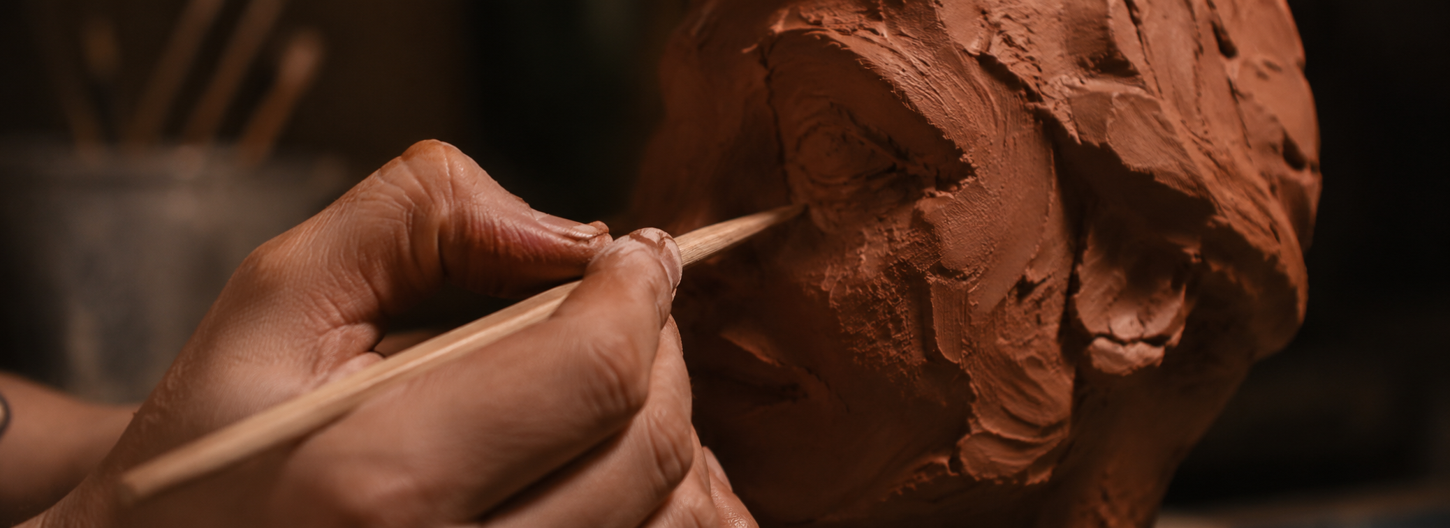 Persona trabajando con palillos en el modelado de una escultura en barro
